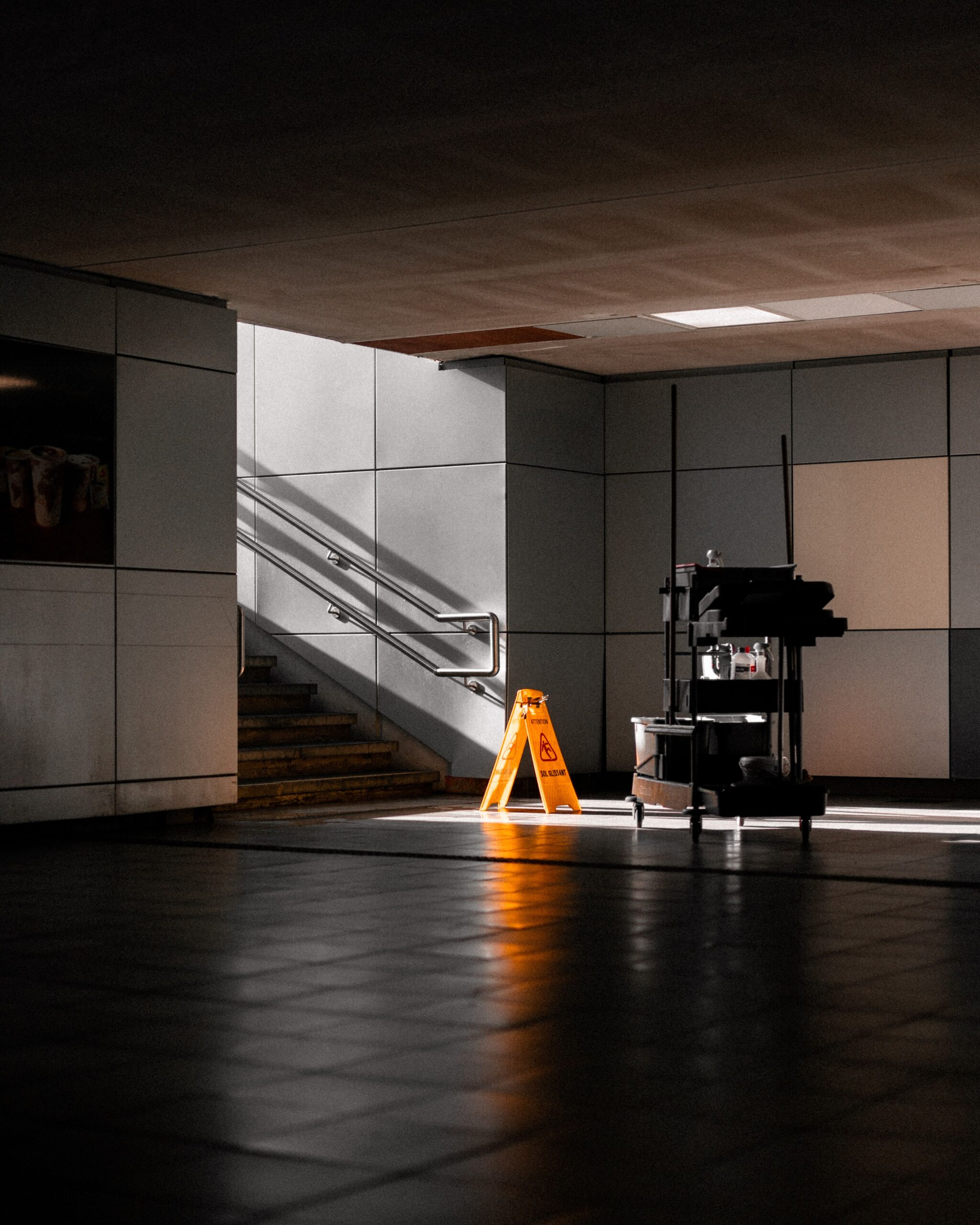 Home A well-lit underground corridor featuring stairs, cleaning supplies, and warning signs.